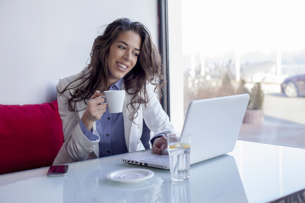 Mujer sonriente tomando un taza café por la mañana y usando una laptop.